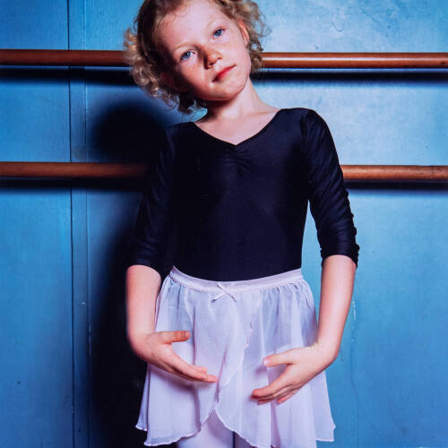 Color photograph of a child wearing ballerina clothing against a blue wall.
